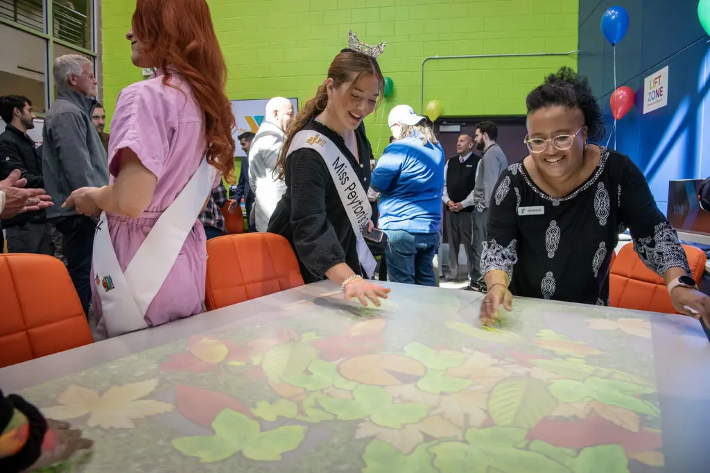 YMCA Lift Zone coordinator Kandace Walker, right, plays a projected touch screen game with Miss Peyton Sofie Leonard following the dedication of the new Lift Zone at the Southeast Armed Services YMCA in Colorado Springs.