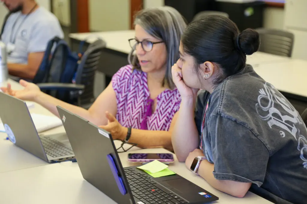 A Digital Navigator demonstrates laptop troubleshooting with a learner in the computer classroom.