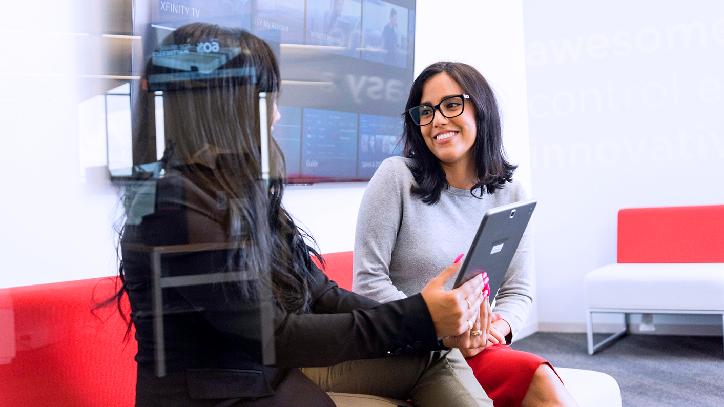 Two coworkers sit next to each other and share a tablet.