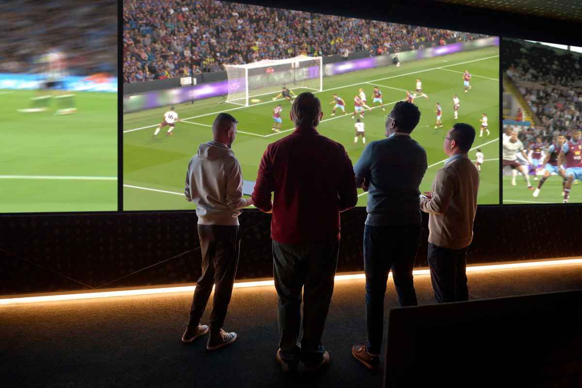 Soccer game playing on a big screen with a group of people watching.